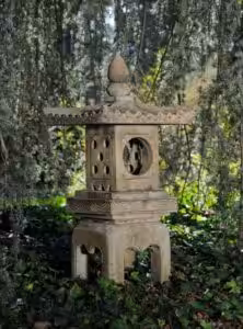 Garden statue of footed Japanese lantern under willow tree