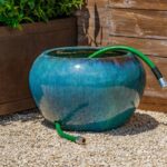 Large blue pottery planter sitting on gravel with holes for garden hose