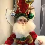 A Mark Roberts fairy, dressed like Santa with ornaments on hat and wearing a red coat
