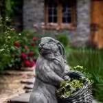 Cast stone planter of rabbit holding a basket containing flowers