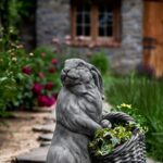 Cast stone planter of rabbit holding a basket containing flowers