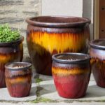 Red, orange, brown glazed pottery planters of different sizes sitting on stone porch