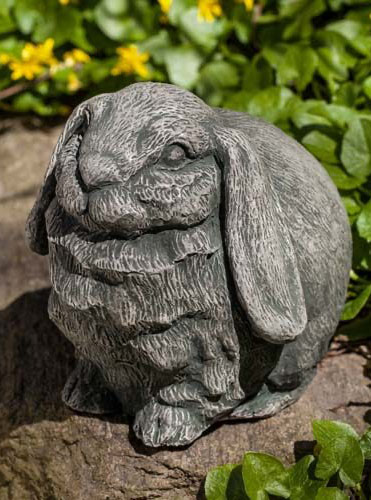 Bunny garden statue sitting on a rock surrounded by green leaves and yellow flowers